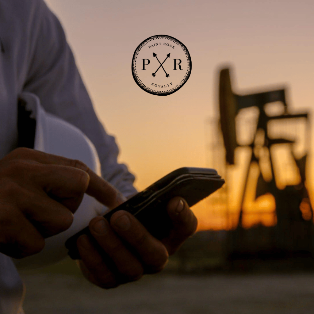 Person using a smartphone in front of an oil pumpjack at sunset with the PXR logo
