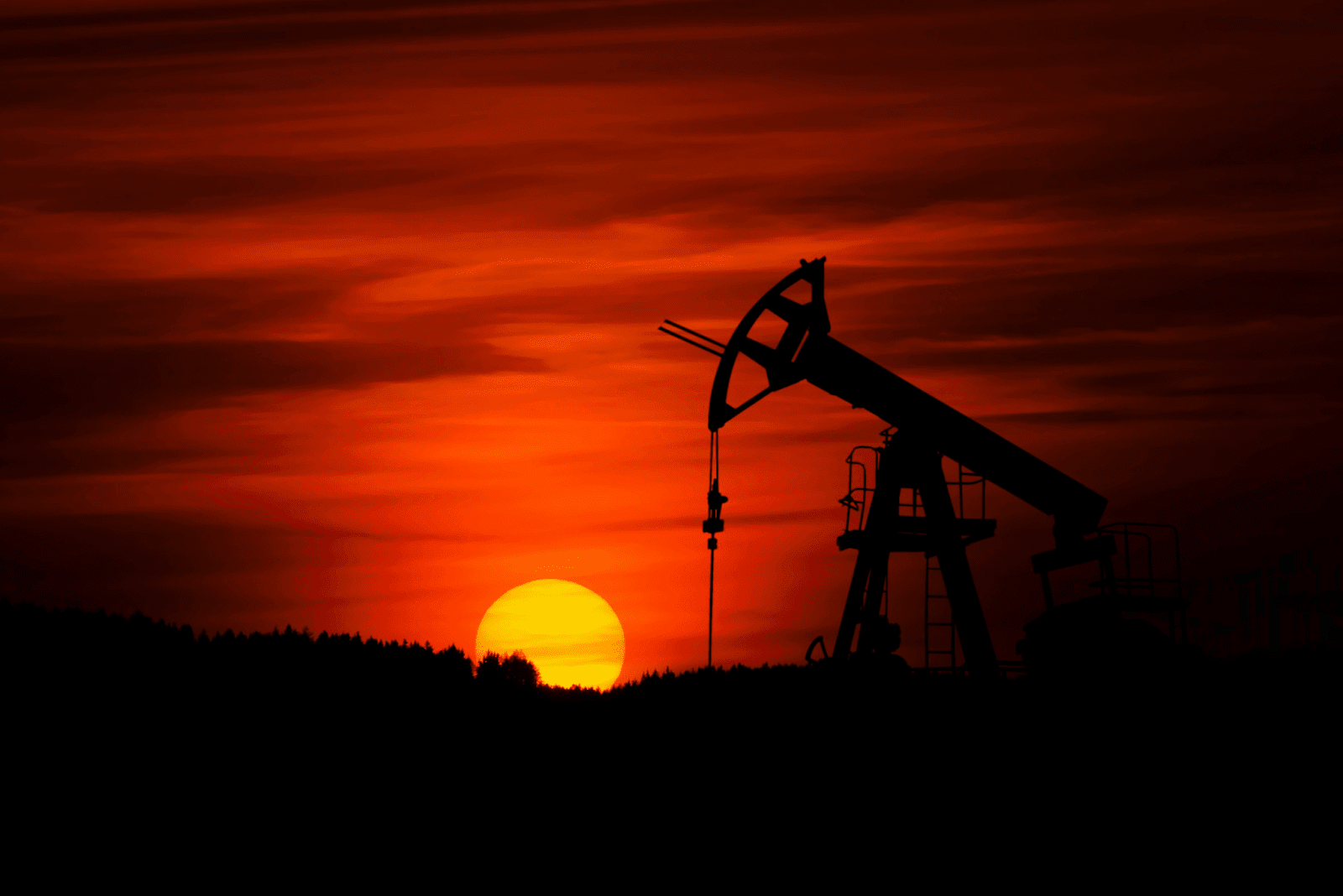 Silhouette of an oil pumpjack against a dramatic red sunset sky.