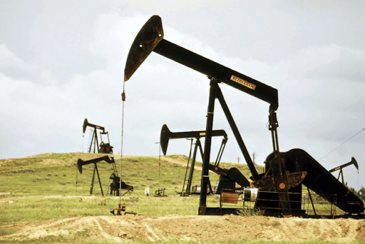 Multiple pumpjack oil rigs operating in a grassy field under a cloudy sky.
