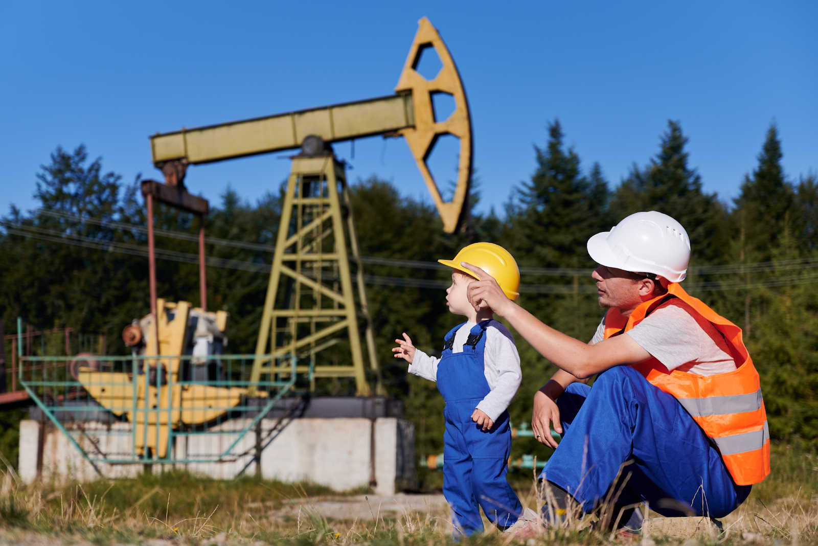 Oil worker and child in safety gear near an oil pumpjack in a rural setting.