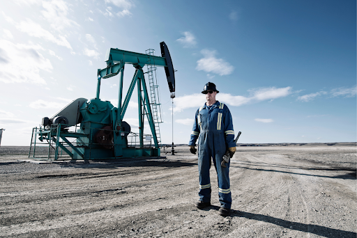 Oil field worker in blue overalls standing in front of a pumpjack on a clear day