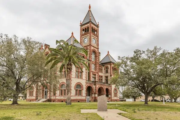 Majestic courthouse with arched windows, palm trees, and a cloudy sky in Cuero, Texas.