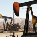 Multiple pumpjack oil rigs operating in a dry landscape with mountains in the background.