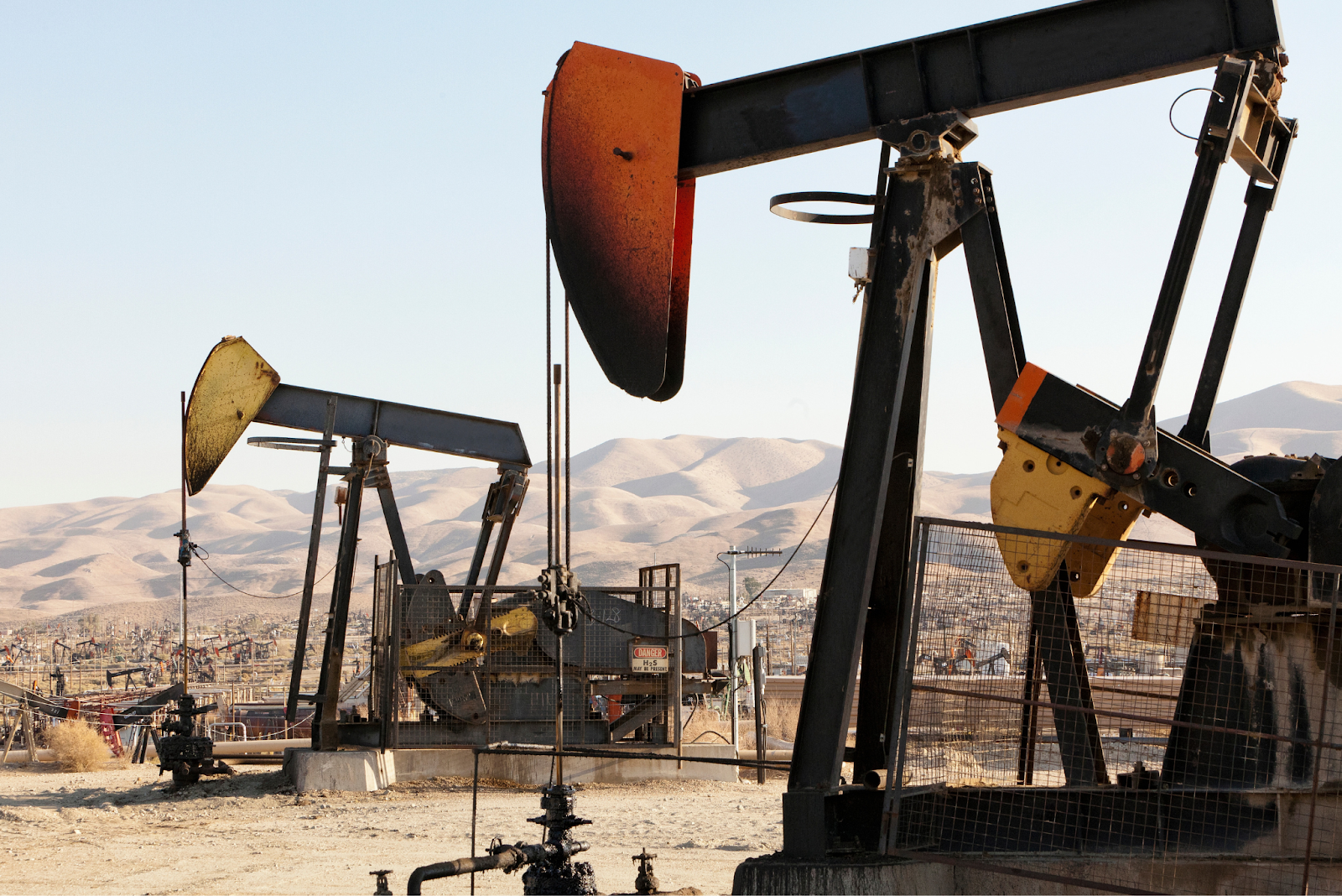 Multiple pumpjack oil rigs operating in a dry landscape with mountains in the background.