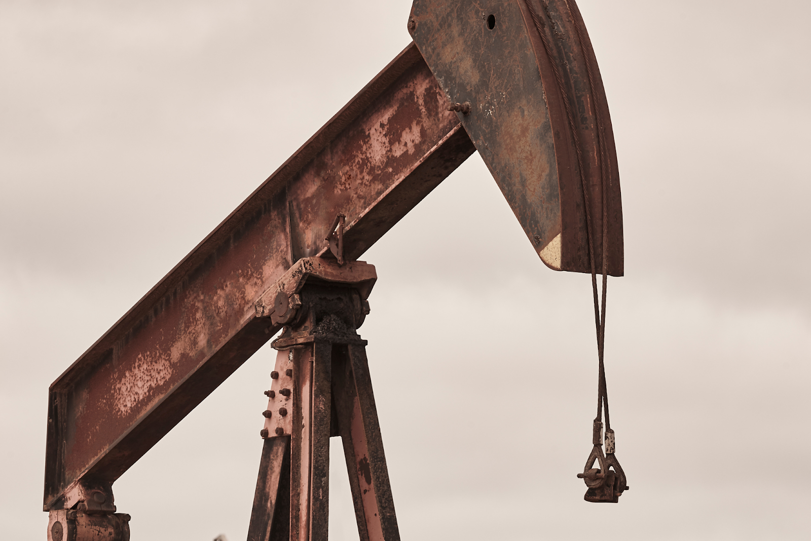 Aging pumpjack oil rig with rusted metal structure under cloudy skies.