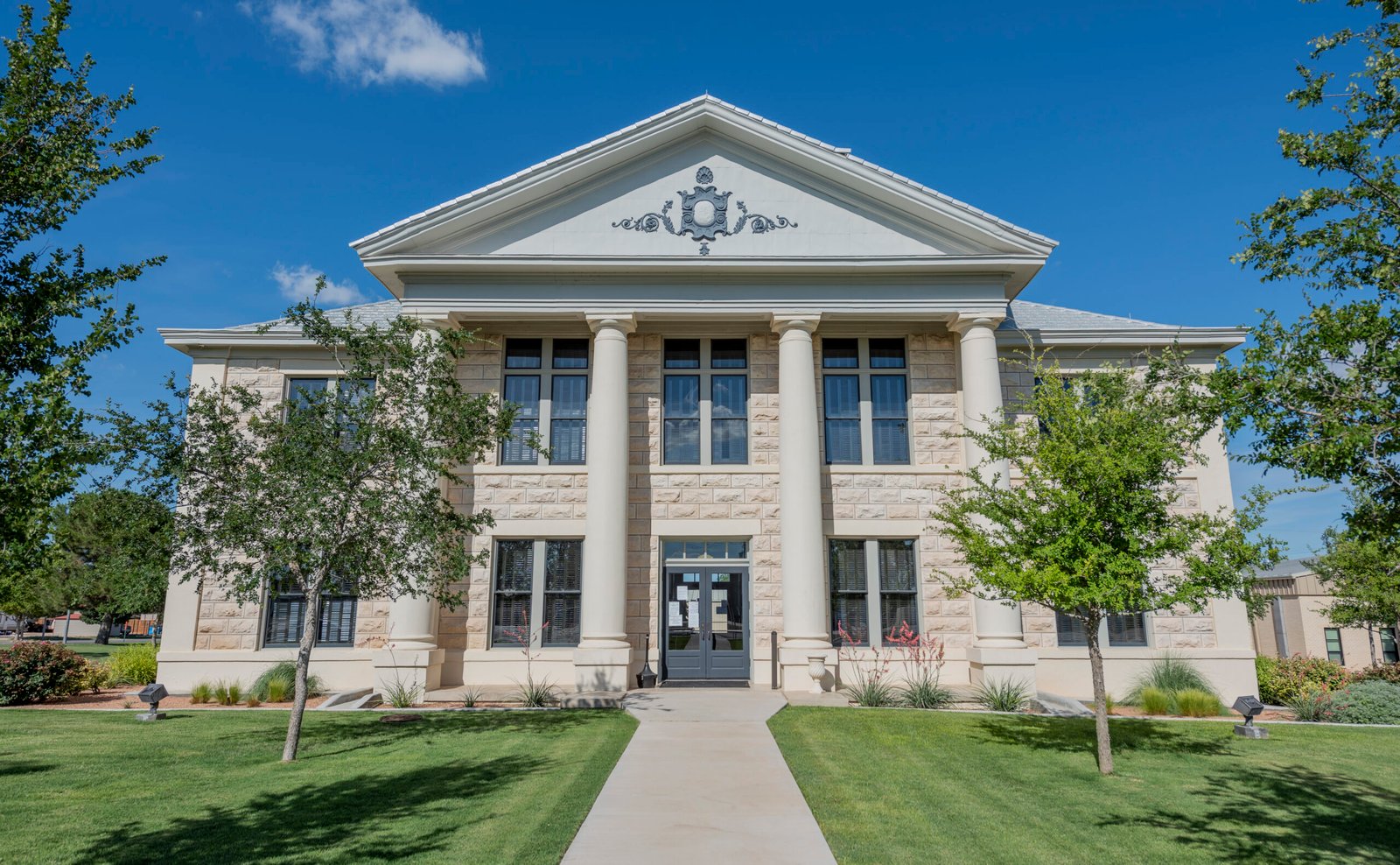 Glasscock County Courthouse, a classic white stone building surrounded by lush greenery and blue skies