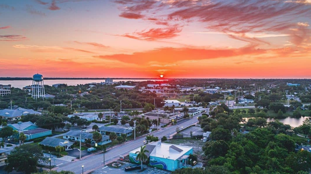Vibrant aerial view of a city skyline at sunset, showcasing a water tower, buildings, and scenic surroundings.