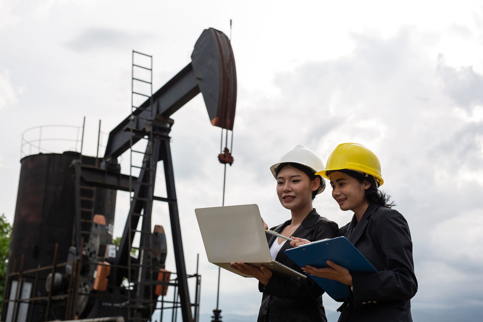 Two female engineers stand beside working oil pumps with a white
